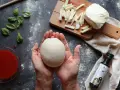 Hände formen Teig für ein Caputo Nuvola Rezept. Mozzarella, Basilikum und Tomatensauce liegen bereit.