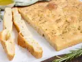 Frisch gebackene Focaccia, ein Klassiker unter den italienischen Brotsorten, mit grobem Salz und Rosmarin bestreut. Daneben liegen zwei geschnittene Stücke.
