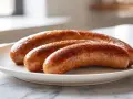 Drei gebratene Salsiccia-Würste liegen auf einem weißen Teller. Sie sind goldbraun und leicht angekohlt, was Appetit auf mehr macht.