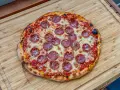 Eine köstliche Pizza Salami mit geschmolzenem Käse und knusprigem Rand liegt auf einem Holzbrett.