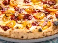 Eine köstliche Nduja Pizza mit geschmolzenem Käse, gelben Tomaten und roten Zwiebeln.