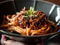 Eine Schüssel mit Pasta und original italienischer Tomatensauce mit Fleisch, garniert mit Parmesan und frischen Kräutern.