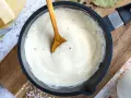 Cremige Béchamelsauce in einer Pfanne, bereit für Lasagne. Butter, Milch und Gewürze liegen daneben.