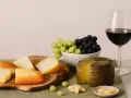 Käseplatte mit verschiedenen Käsesorten, Trauben und einem Glas Rotwein. Was bedeutet Primitivo bei Wein? Oft ein vollmundiger, fruchtiger Rotwein, der gut zu Käse passt.
