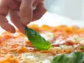 Eine Hand belegt eine Pizza mit frischem Basilikum. Die Pizza belegen reihenfolge ist wichtig für den perfekten Geschmack.
