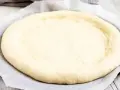 Ein runder, flacher Pizzaboden aus einem Pizzateig Rezept mit frischer Hefe, bereit für Belag und Backen.