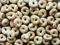 Viele goldbraune Taralli, die nach einem einfachen Taralli Rezept gebacken wurden, liegen dicht beieinander auf dunklem Holz.