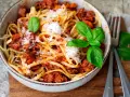 Eine Schüssel mit Linguine und einer herzhaften, **schnellen Bolognese**, garniert mit frischem Basilikum und Parmesan.
