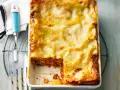 Eine frisch gebackene Lasagne al Ragu, goldbraun überbacken, wartet darauf, serviert zu werden. Ein Stück wurde bereits entnommen.