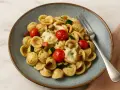 Orecchiette-Nudeln mit Kirschtomaten, Zucchini und geschmolzenem Käse. Die Aussprache von Orecchiette ist "oh-reh-KYET-teh".