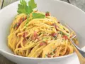Spaghetti Carbonara mit knusprigem Schinken, garniert mit Petersilie und schwarzem Pfeffer, serviert in einer weißen Schüssel.