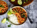 Herzhafte Kichererbsen Rezepte: Ein Teller mit Reis und Kichererbsen-Curry, garniert mit Limettenspalten und Koriander.