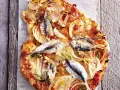Eine rustikale Sardellen Pizza mit Zwiebeln und grünen Paprikastreifen, auf einem Holzbrett serviert.