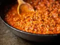 Herzhafte Bolognese-Sauce köchelt in einer Pfanne, die Zutaten für ein perfektes Pastagericht. Ein Holzlöffel rührt die köstliche Masse.