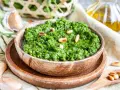 Frisches Rucola Pesto, garniert mit Pinienkernen, daneben Knoblauch und Olivenöl.