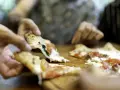 Hände greifen nach dampfenden Pizzastücken. So wie essen Italiener Pizza: gemeinsam, genussvoll, mit Freunden.