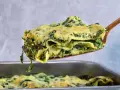 Ein Stück cremiger Ricotta Spinat Lasagne wird aus einer Auflaufform gehoben.