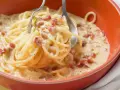 Cremige Pasta mit Ei und Speckwürfeln, ein klassisches italienisches Gericht, serviert in einer orangen Schüssel.