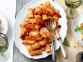Ein Teller mit Rigatoni mit Tomatensauce, garniert mit Parmesan und Basilikum. Daneben ein Glas Weißwein.
