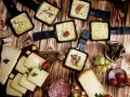 Raclette-Pfännchen mit geschmolzenem Käse, dazu Brot, Käse, Salami, Cornichons und Trauben. Perfekt für einen gemütlichen Abend mit **Wein zum Raclette**.