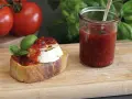 Bruschetta mit Ziegenkäse und Tomatenmarmelade, inspiriert von einem italienischen Tomatenmarmelade Rezept. Frische Tomaten und Basilikum im Hintergrund.