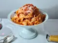 Ein Teller breiter Bandnudeln mit herzhaftem al ragu, bestreut mit Parmesan. Daneben ein Glas Rotwein und Besteck.