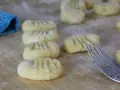 Frisch geformte italienische Gnocchi liegen auf bemehltem Holz. Eine Gabel und ein blauer Lappen sind ebenfalls zu sehen.