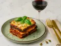 Ein köstlicher Auberginenauflauf italienisch, garniert mit Basilikum, neben einem Glas Rotwein und goldenem Besteck.