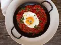 Ein Spiegelei ruht in einer würzigen Tomatensoße, garniert mit Kräutern und Käse. Ein Gericht, das an "uova in purgatorio" erinnert.