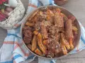Herzhaftes Pasta Ragu mit Fleischstücken und geriebenem Käse, serviert in einer Schüssel auf einem karierten Tuch. Daneben ein Korb mit Knoblauch, Schalotten und Chilis.