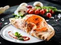 Ein goldbrauner, knuspriger Pizza Calzone mit geschmolzenem Käse und frischem Basilikum auf einem Teller.