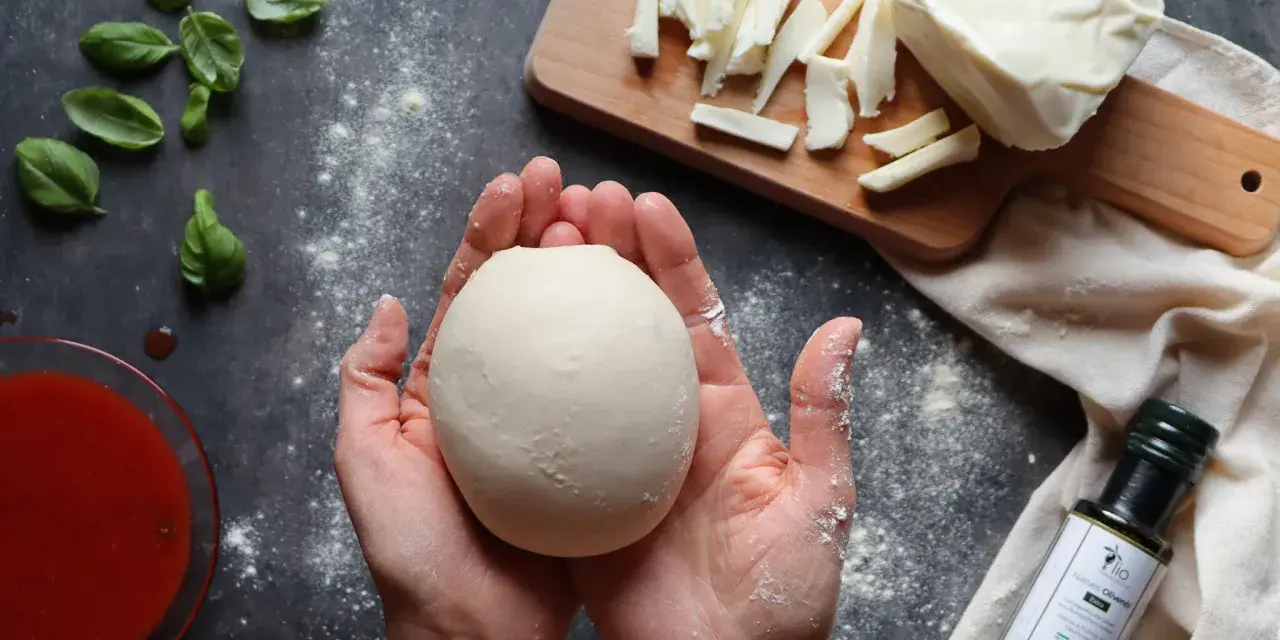 Hände formen Teig für ein Caputo Nuvola Rezept. Mozzarella, Basilikum und Tomatensauce liegen bereit.