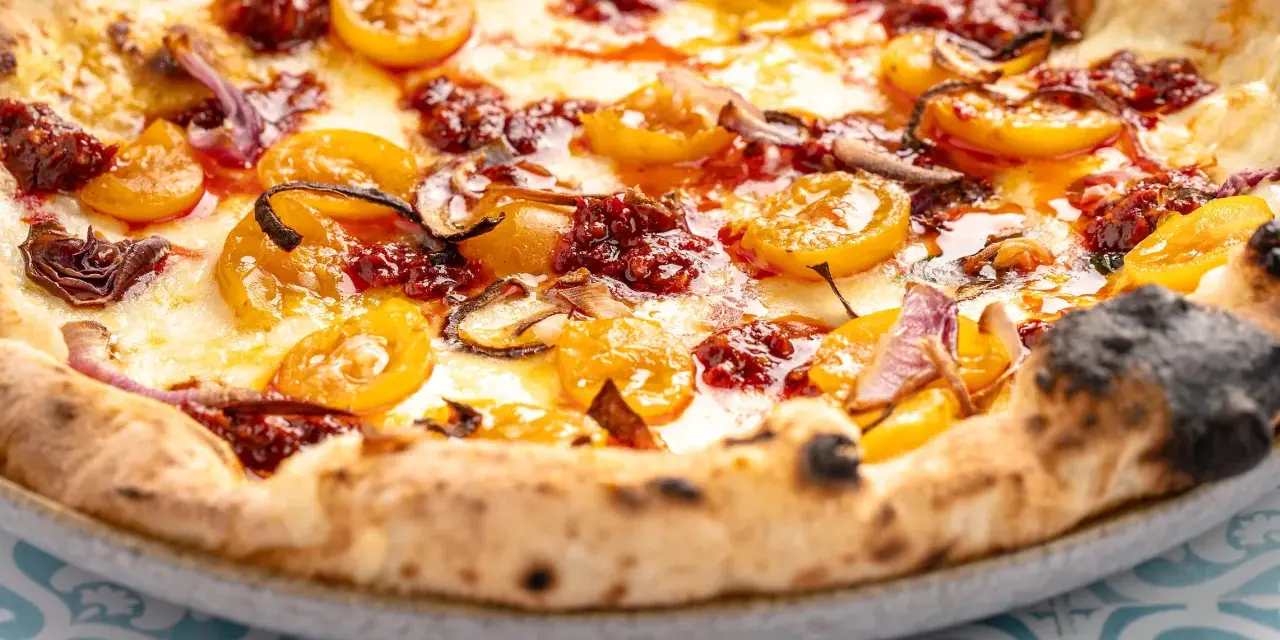 Eine köstliche Nduja Pizza mit geschmolzenem Käse, gelben Tomaten und roten Zwiebeln.