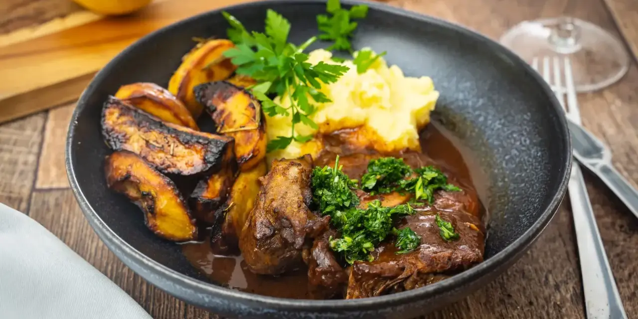 Ein Teller mit dem originalen Ossobuco-Rezept, dazu Kartoffelpüree und geröstete Kartoffelspalten.