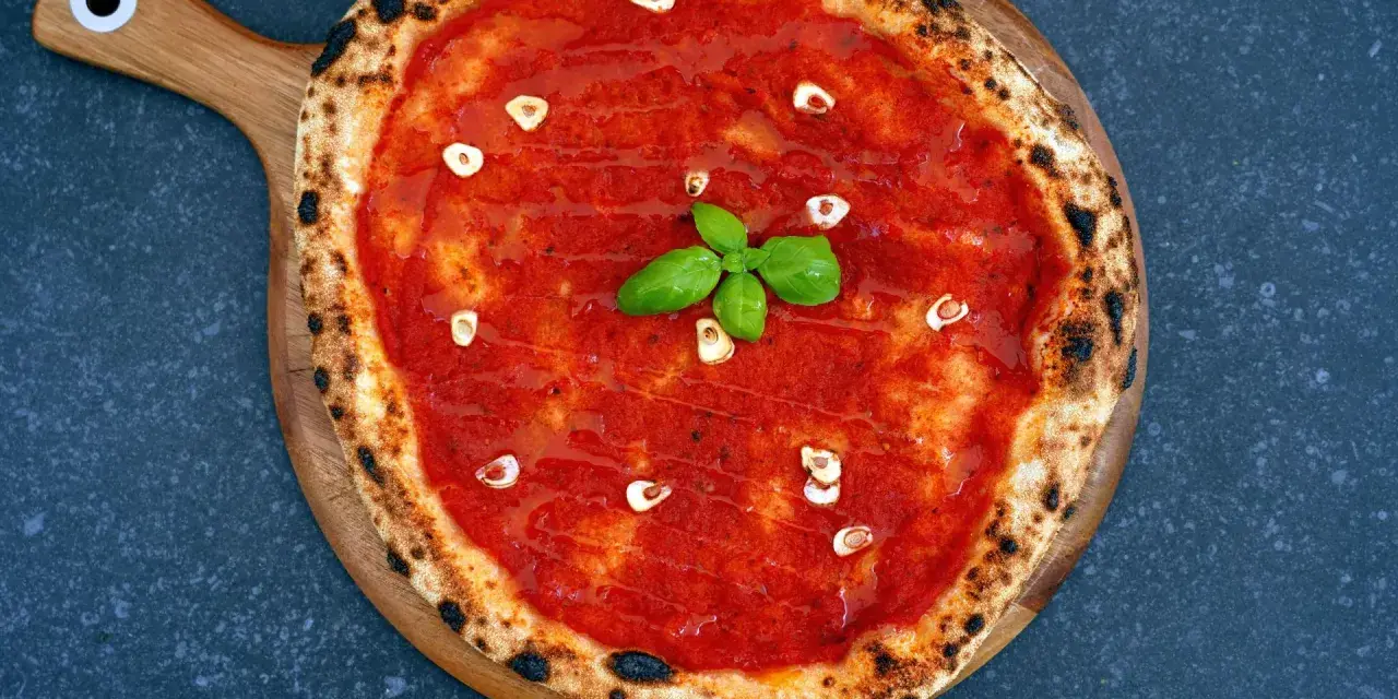 Eine klassische Pizza Marinara mit Tomatensauce, Knoblauch und frischem Basilikum auf einem Holzbrett.