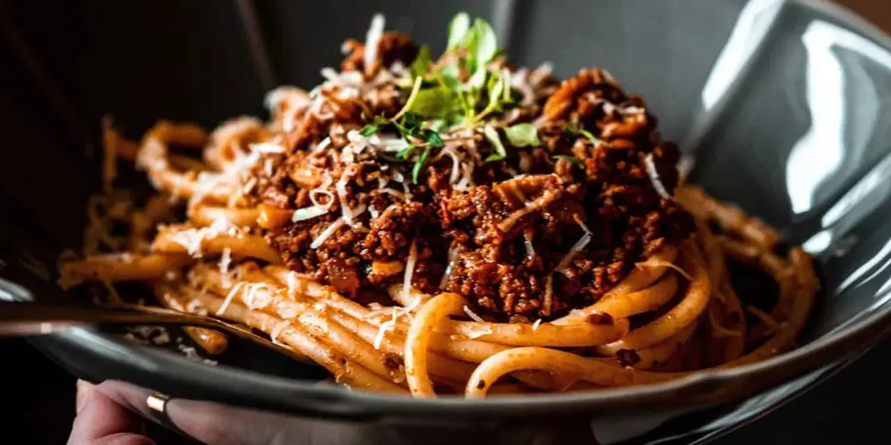 Eine Schüssel mit Pasta und original italienischer Tomatensauce mit Fleisch, garniert mit Parmesan und frischen Kräutern.