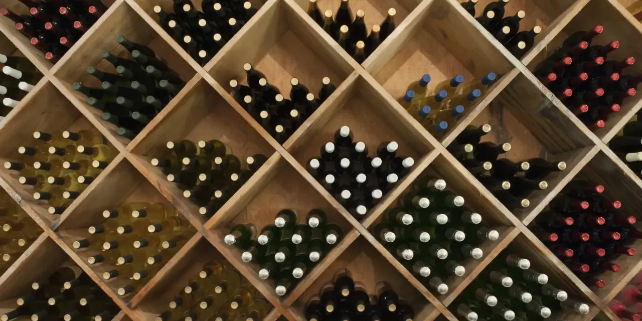 Weinregal mit vielen Flaschen Wein. Die Frage, wie lange kann man Wein lagern, hängt von der Sorte ab.