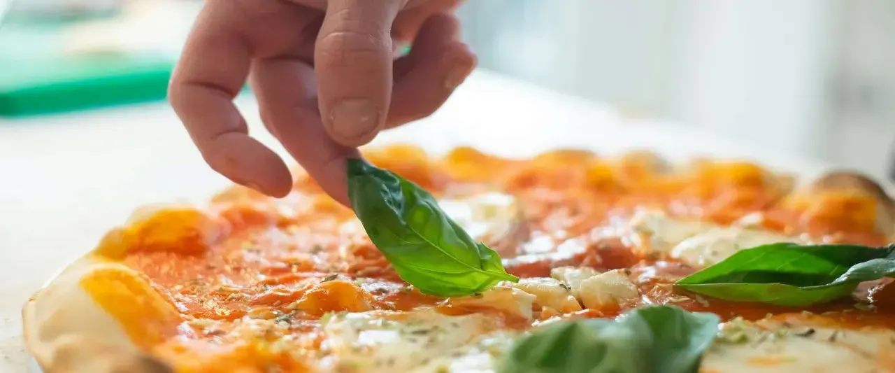 Eine Hand belegt eine Pizza mit frischem Basilikum. Die Pizza belegen reihenfolge ist wichtig für den perfekten Geschmack.