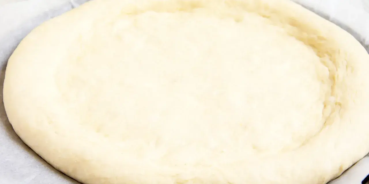 Ein runder, flacher Pizzaboden aus einem Pizzateig Rezept mit frischer Hefe, bereit für Belag und Backen.