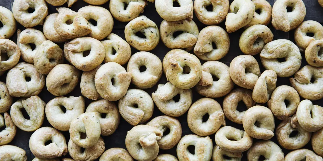 Viele goldbraune Taralli, die nach einem einfachen Taralli Rezept gebacken wurden, liegen dicht beieinander auf dunklem Holz.