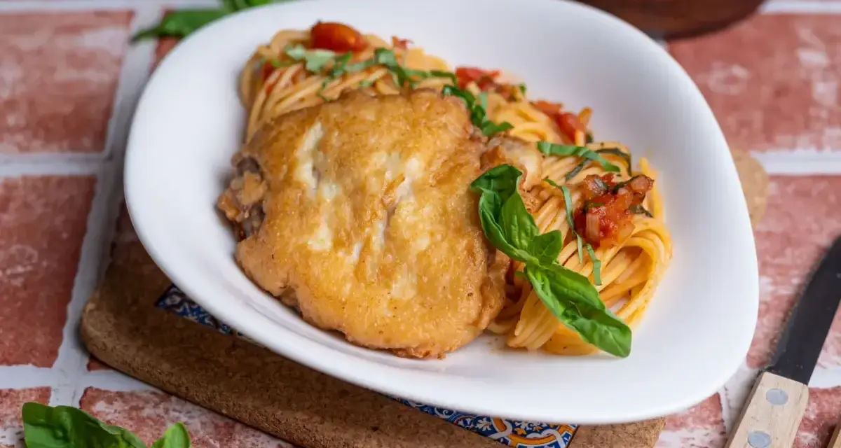 Ein paniertes Hähnchenfilet auf Spaghetti mit Tomatensoße und Basilikum. Ein Gericht, das an Piccata erinnert, aber ohne Zitrone.