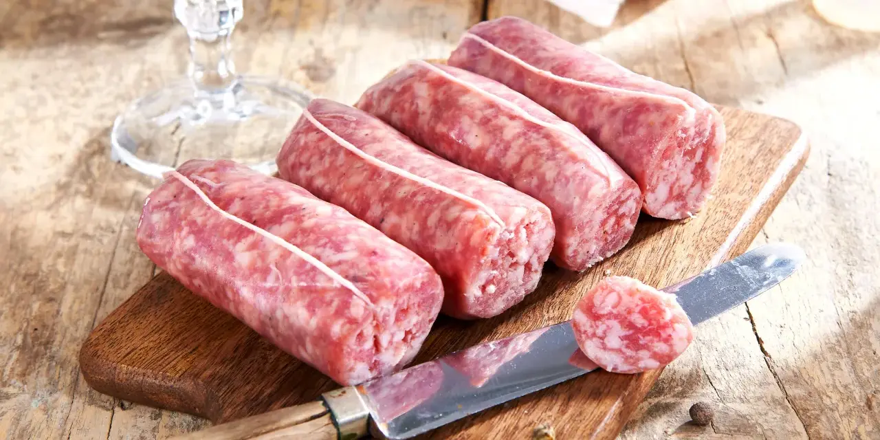 Frische Salsiccia zum Zubereiten liegen auf einem Holzbrett. Ein Messer mit einer Scheibe daneben deutet auf die Vorbereitung hin.