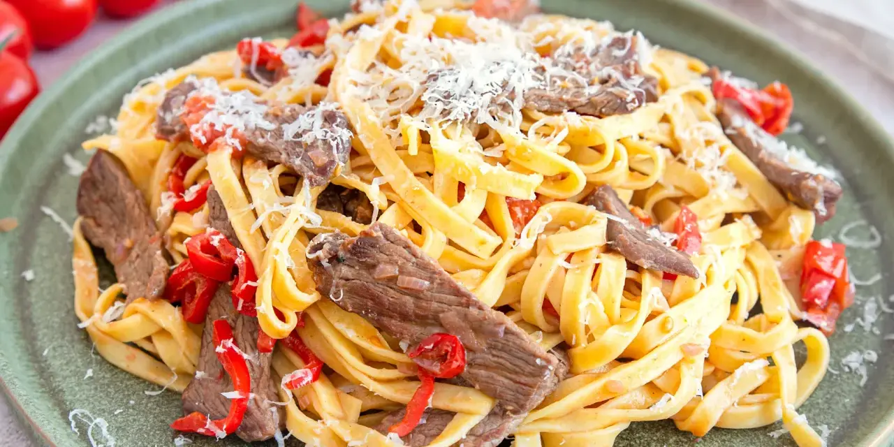 Pasta mit Rinderfiletstreifen, Tomaten und Parmesan auf einem grünen Teller.