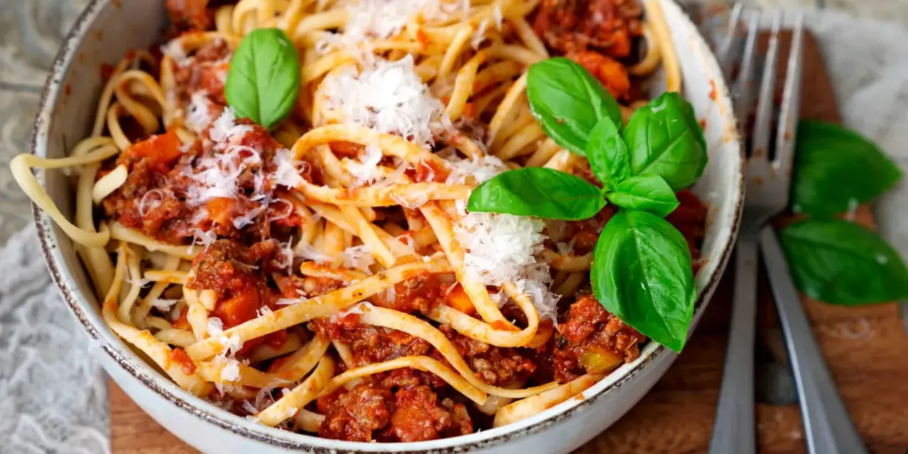 Eine Schüssel mit Linguine und einer herzhaften, **schnellen Bolognese**, garniert mit frischem Basilikum und Parmesan.