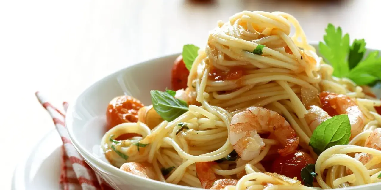 Ein Teller mit köstlichen Spaghetti mit Garnelen, Kirschtomaten und frischem Basilikum, appetitlich angerichtet.