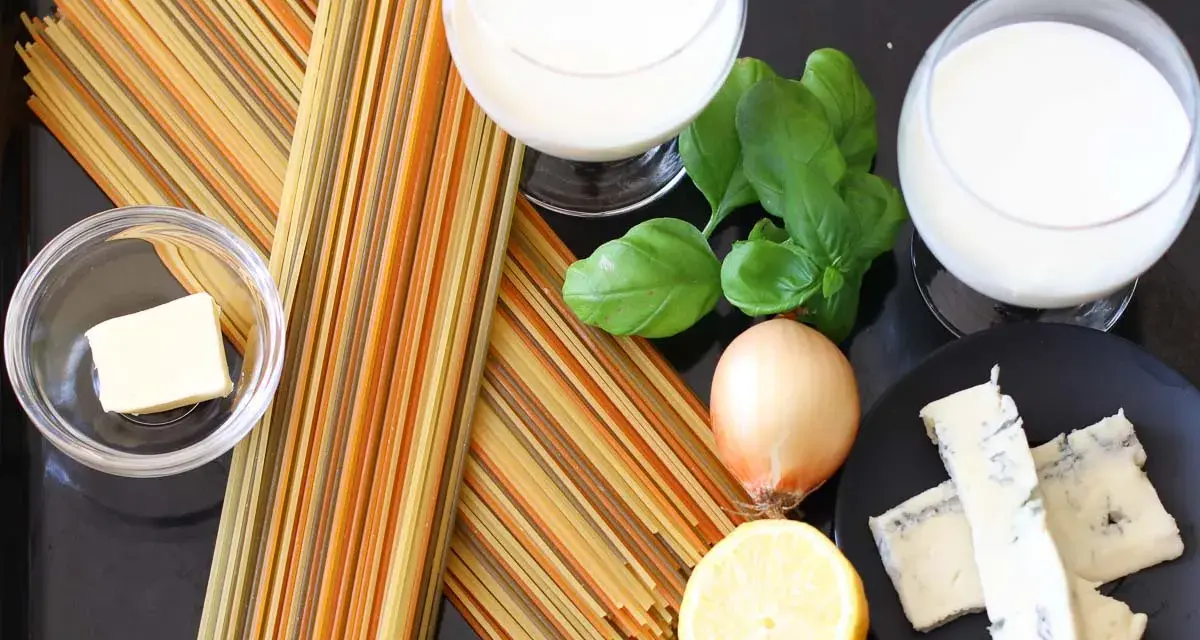 Zutaten für eine cremige Gorgonzola-Sauce: bunte Spaghetti, Butter, Zwiebel, Zitrone, Basilikum und Gorgonzola.