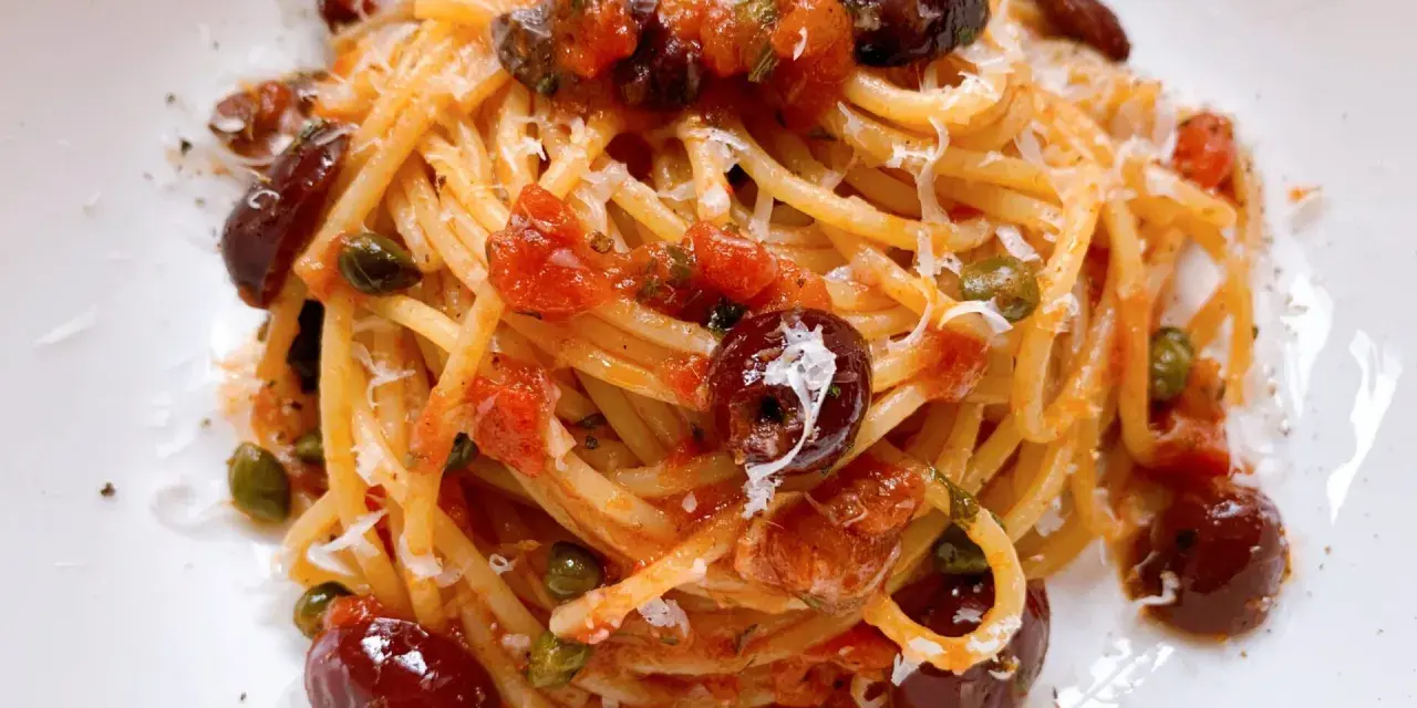 Ein Teller Spaghetti Puttanesca, garniert mit Oliven, Kapern und Parmesan.
