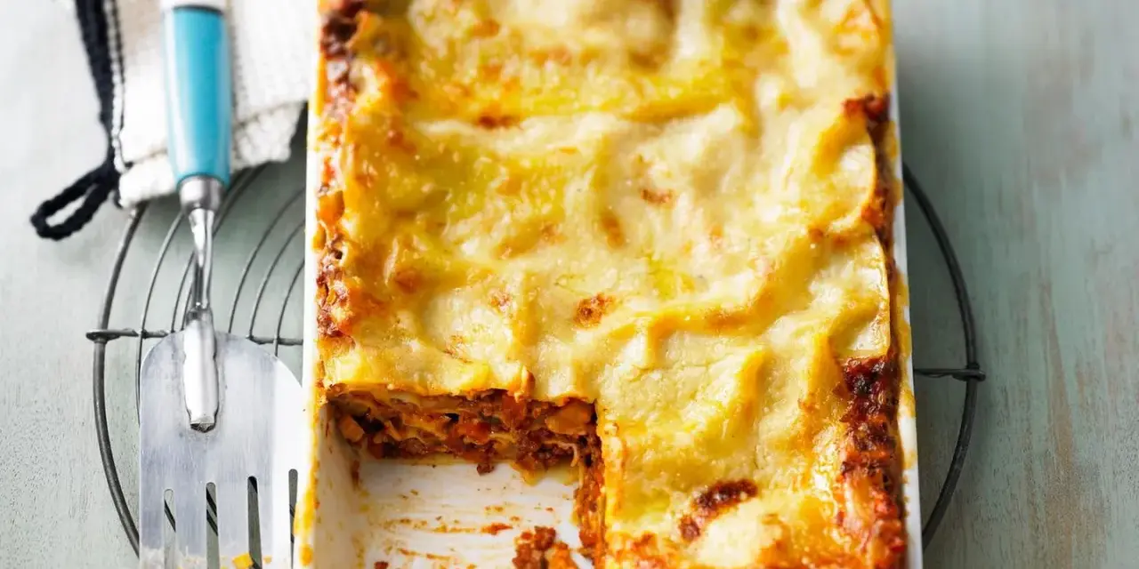 Eine frisch gebackene Lasagne al Ragu, goldbraun überbacken, wartet darauf, serviert zu werden. Ein Stück wurde bereits entnommen.