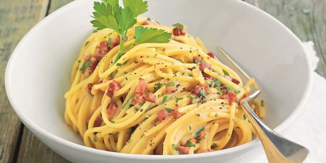 Spaghetti Carbonara mit knusprigem Schinken, garniert mit Petersilie und schwarzem Pfeffer, serviert in einer weißen Schüssel.