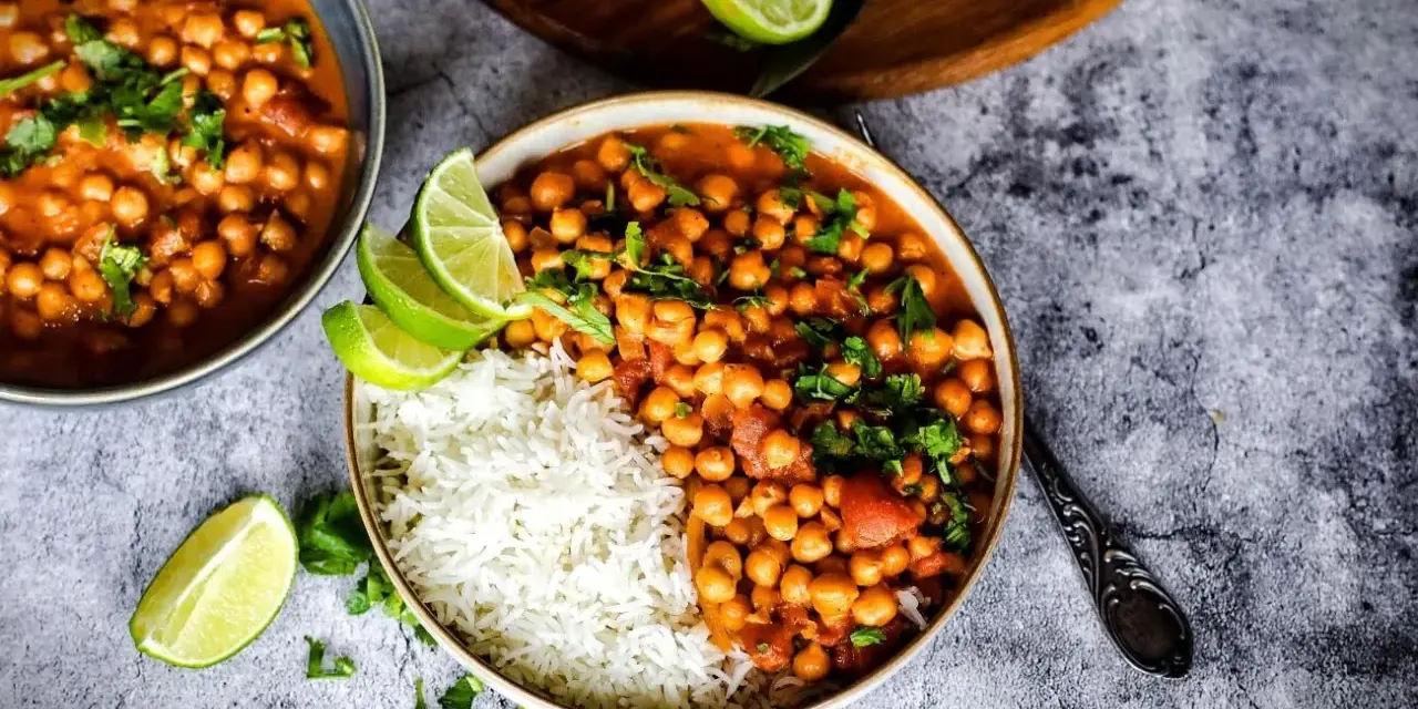 Herzhafte Kichererbsen Rezepte: Ein Teller mit Reis und Kichererbsen-Curry, garniert mit Limettenspalten und Koriander.